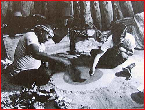 Le chaman et un assistant font couler le sable entre le pouce et l'index, jusqu' a la fin de la peinture de sable...