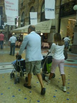 due genitori con due bambini e due passeggini visti da dietro