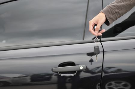 male hand holding car key with new black car in background